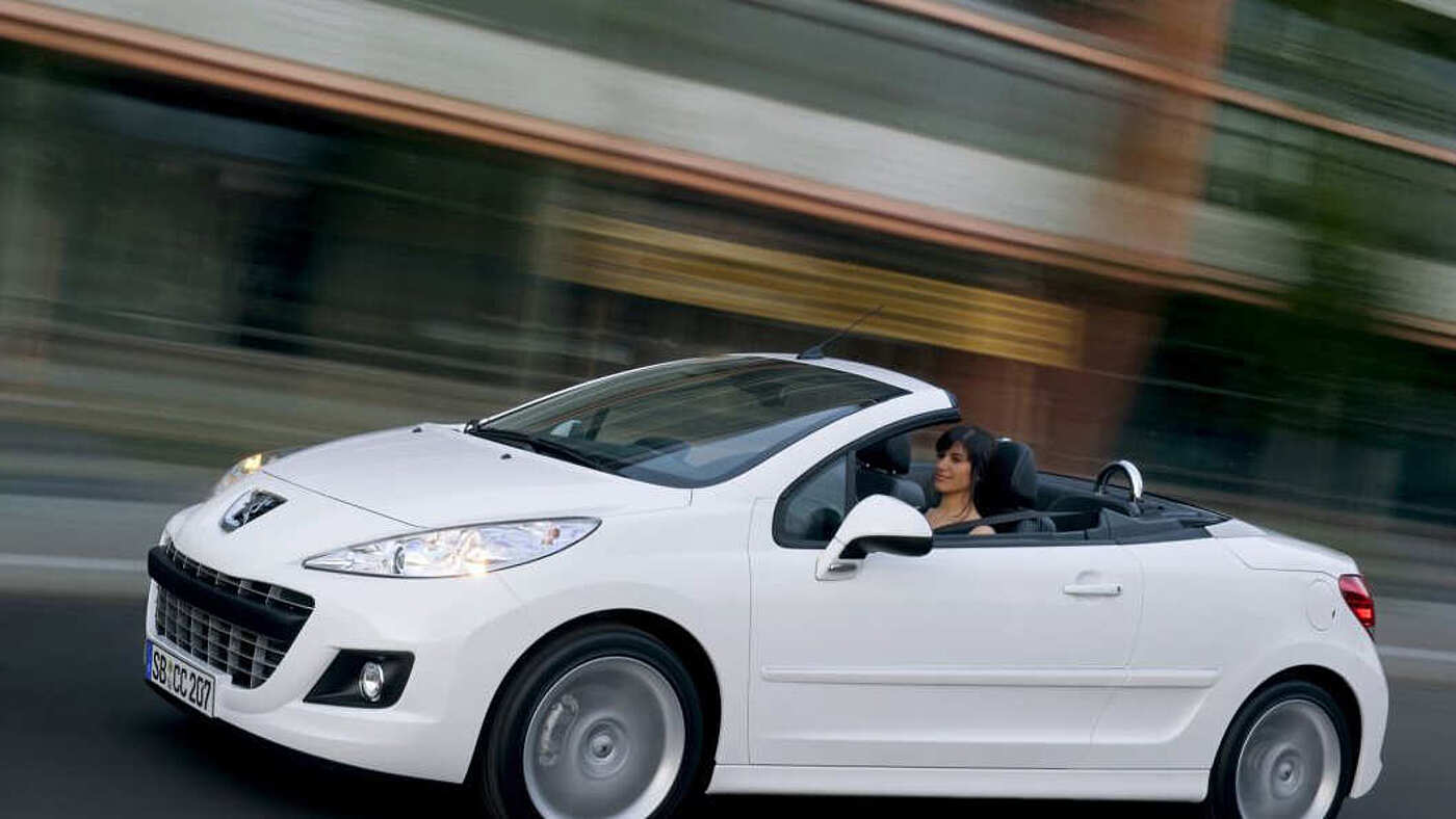 Der Peugeot 207 in Wei&szlig; mit offenem Verdeck in der Seitenansicht bei der Fahrt.